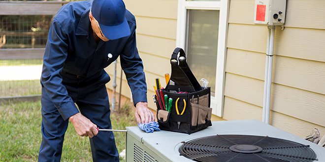 Technician in blue uniform repairing an outdoor HVAC unit with a toolkit nearby.