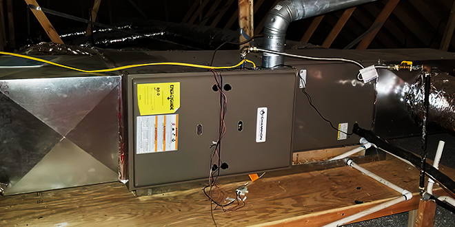 HVAC unit installed in an attic, with visible ductwork and wiring on a wooden platform.
