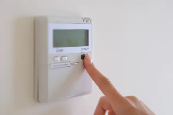 The Cost of AC Installation: What to Expect and How to Budget for It - Female finger pressing air conditioner button on wall.