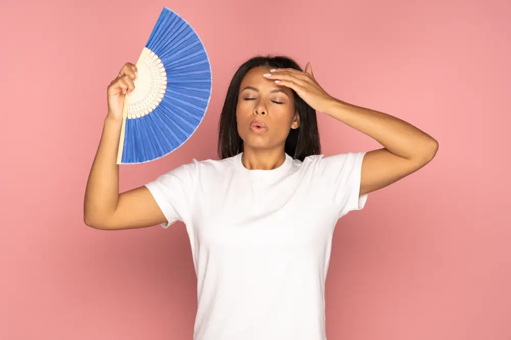 Tackling Hot Weather AC Issues in Searcy's Sizzling Summers - Exhausted african woman using paper fan suffer from heat sweating, feels sluggish isolated on pink.