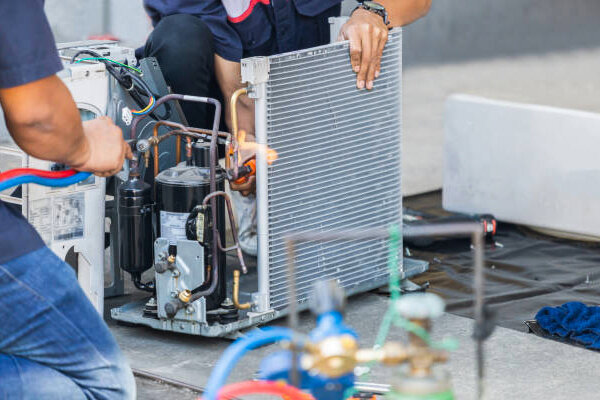 Technicians repairing an air conditioning unit with tools and gauges.