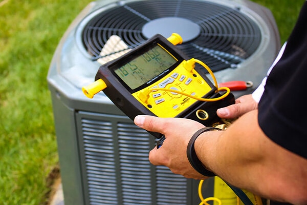 Technician using a digital gauge to check an outdoor air conditioning unit.