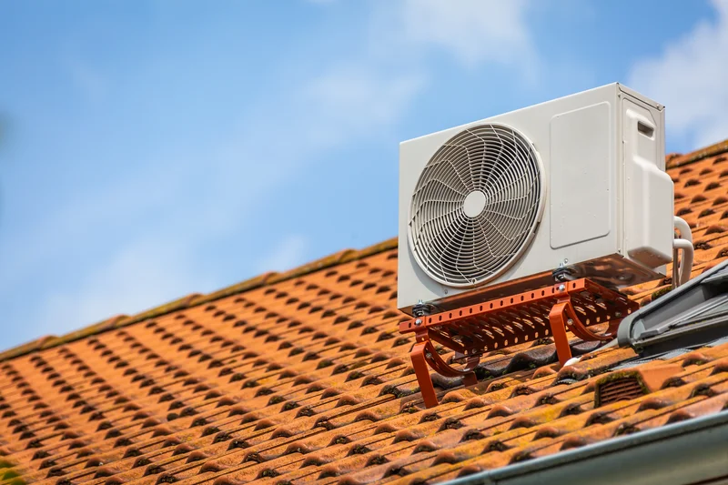 Rooftop air conditioning unit on red roof tiles under a clear blue sky.