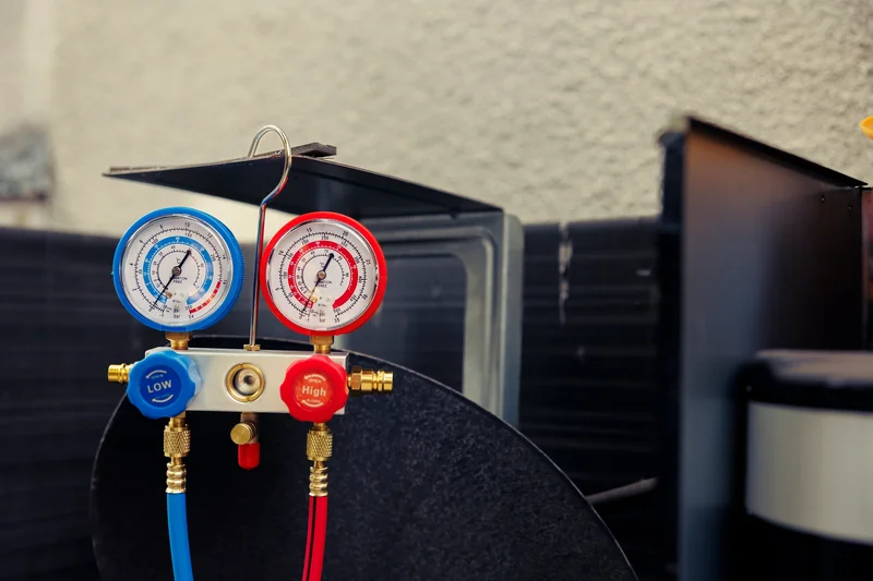 HVAC pressure gauges with blue and red dials attached to pipes against a utility backdrop.