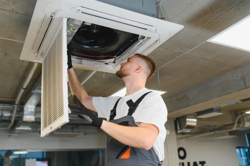 Technician in uniform inspecting a ceiling-mounted air conditioning unit.