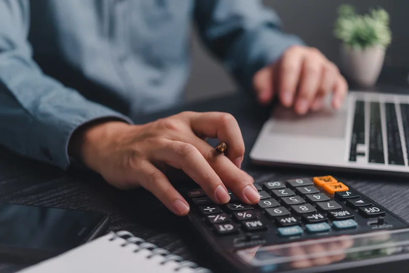 Person using a calculator and laptop on a desk.