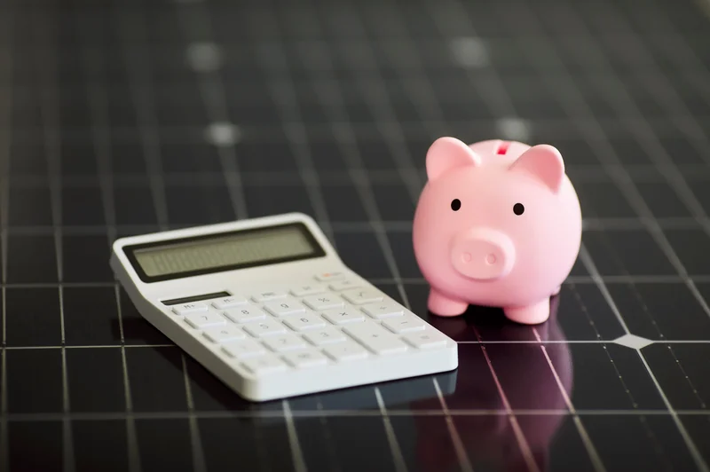 Pink piggy bank and white calculator on a grid-patterned surface.